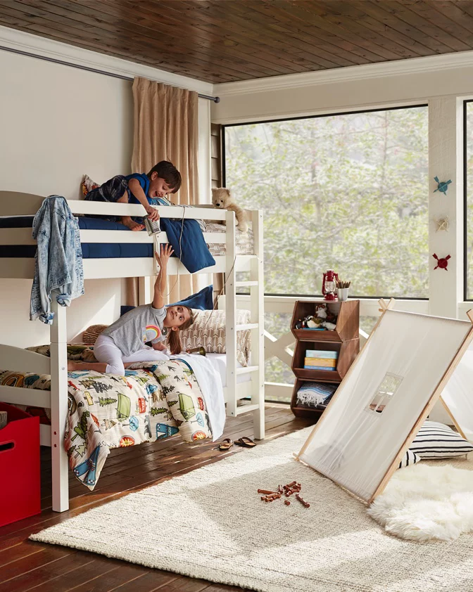 A kids' room inspired by summer camps with a bunk bed, tents, log pillows, pennant flags, and more. 