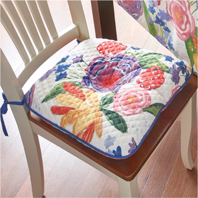 A floral chair pad by The Pioneer Woman tied to a wooden dining chair. 