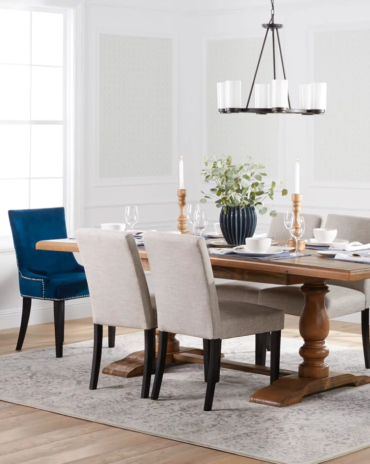 A transitional dining room with a beautiful wooden trestle table, upholstered seating, blue velvet end chairs, an industrial chandelier and a dining table area rug. Links to Payless Daily's dining room furniture and decor